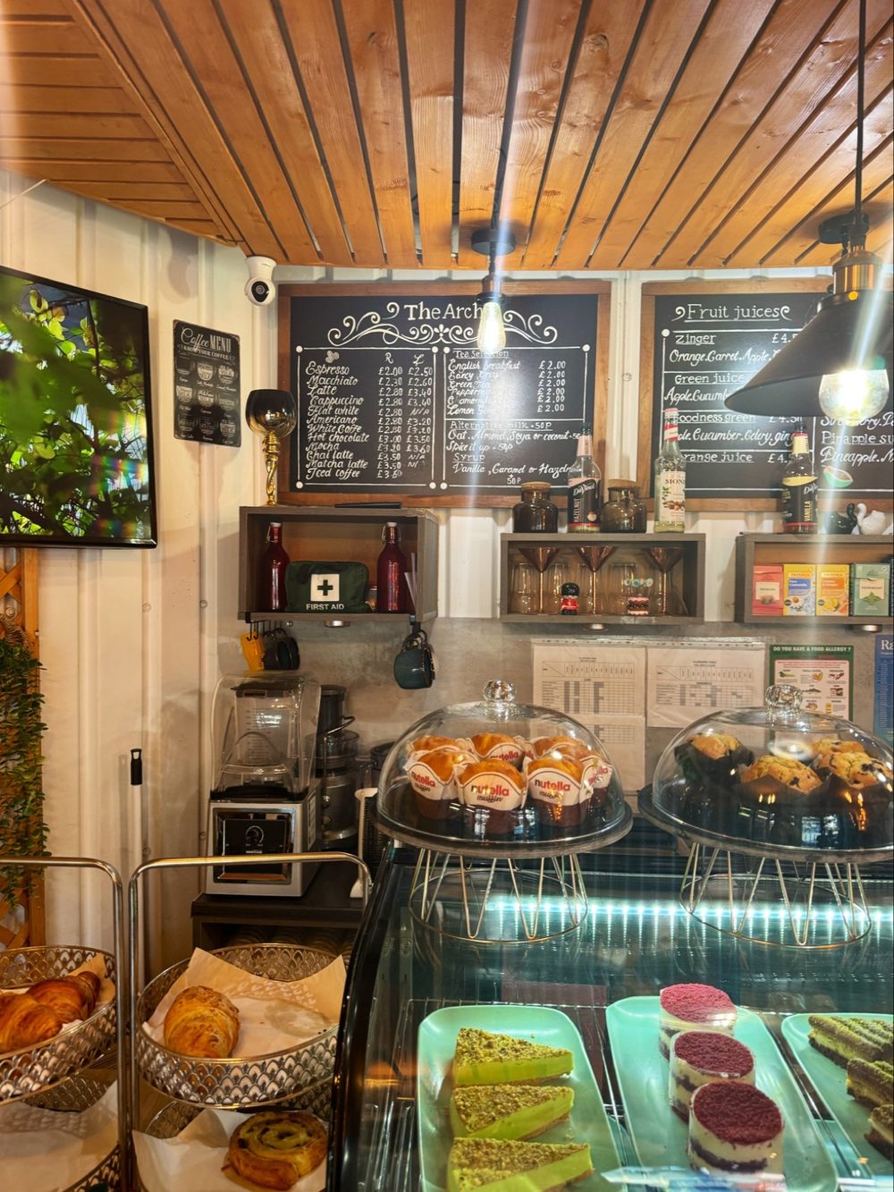 Inside the cafe looking towards the counter, with a cake and pastry display case under a timber-clad ceiling