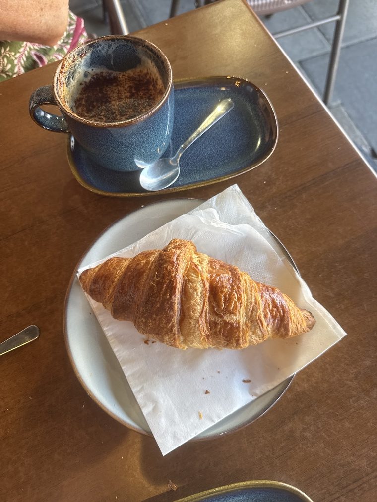 An espresso in a blue glazed cup beside a croissant, shot from above